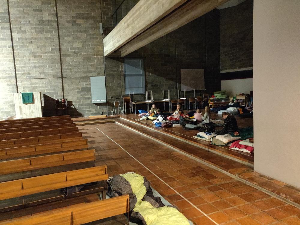 Kuva Huutoniemen kirkosta. Levitettynä makuualustoja sekä makuupusseja. Niiden päällä istuu lapsia.