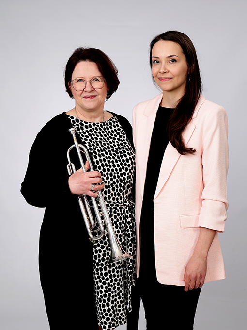Kaksi kanttorit seisovat vieretysten ja hymyilevät. Toisella kädessään torvisoitin.
