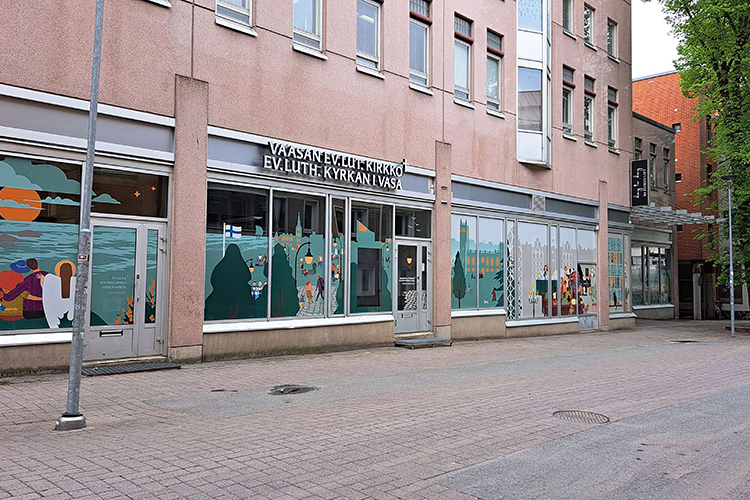 Vaaleanpunainen rakennus, jossa isoja värikkäilä teippauksilla koristetuja ikkunoita. 