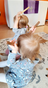 Lapset istuvat lattialla ja soittavat rytmikapuloilla.