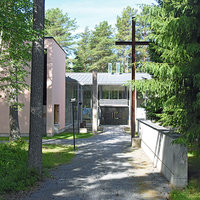 Gerbyn seurakuntakoti Metsänreunassa sijaitsevan talon sissänkäynti. Pihalla iso risti.