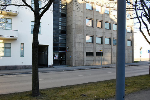 Harmaa kerrostalos kadun vieressä.
