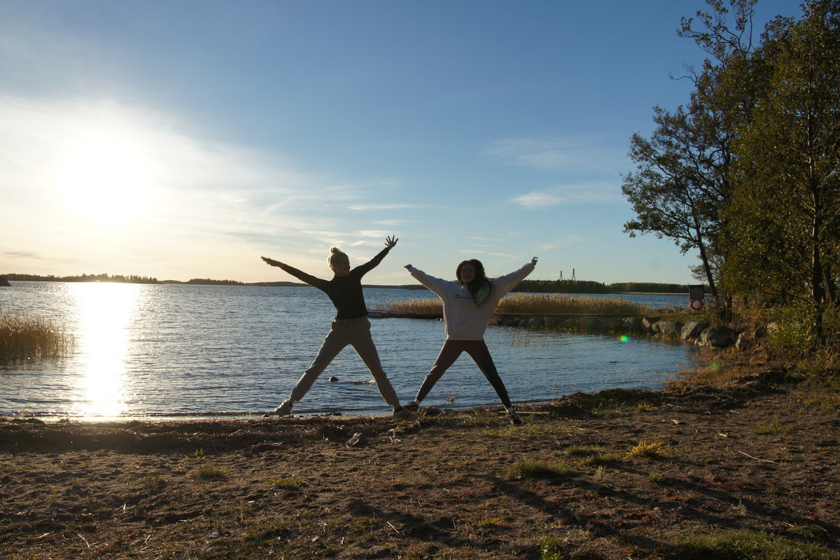 Kaksi tyttöä hyppää korkealle meren rannalla auringon laskiessa taustalla.