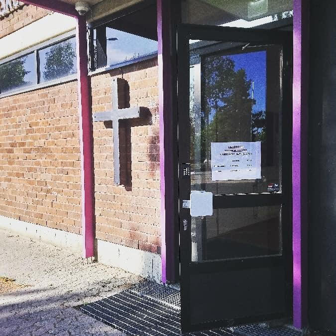 Ristinummen seurakuntakeskuksen avoin ulko-ovi. Ulkoseinässä risti.